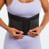 A woman in a light purple workout set wearing the 5350 Double Pull Back Brace around her lower back with her hands of either side of her belly button where the tabs are. The brace is secured with adjustable double closures and provides support to her lower back, highlighting the flexible posterior stays and the 8-inch width for targeted support.